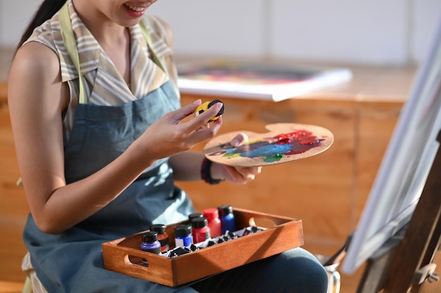 Lächelnde asiatische Frau, die eine Palette hält, während sie in ihrem Atelier an der Malerei arbeitet