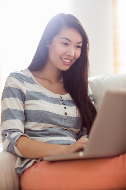 Lächelnde asiatische Frau, die Laptop auf Couch verwendet