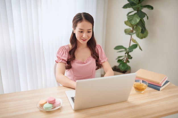 Lächelnde asiatische Frau, die zu Hause Laptop verwendet. Freiberufler.