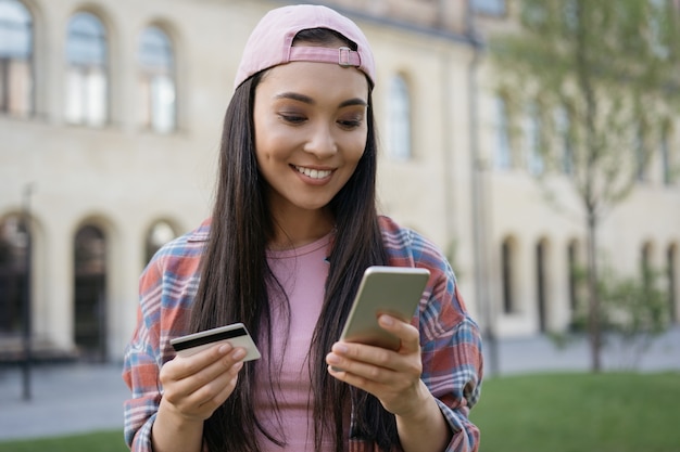 Lächelnde asiatische Frau mit Handy mit Kreditkarte online einkaufen