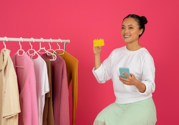 Lächelnde asiatische Frau mit Kreditkarte und Smartphone-Werbung für Online-Shopping-App