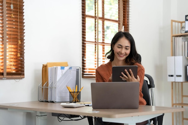 Lächelnde asiatische Frau steht mit modernem Pad-Gadget zu Hause beim Surfen im Internet oder beim Einkaufen. Glückliche zufriedene junge Kundin surft im Internet, liest Nachrichten oder chattet auf Tablet-Gerät-Technologiekonzept