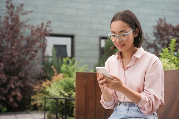 Lächelnde asiatische Geschäftsfrau, die Handy hält, E-Mails checkt, SMS liest