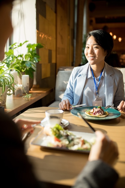 Foto lächelnde asiatische geschäftsfrau, die mit freund zu mittag isst