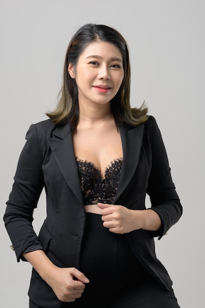 Lächelnde asiatische Geschäftsfrau, die nach oben zeigt und die Kamera über grauem Hintergrund betrachtet