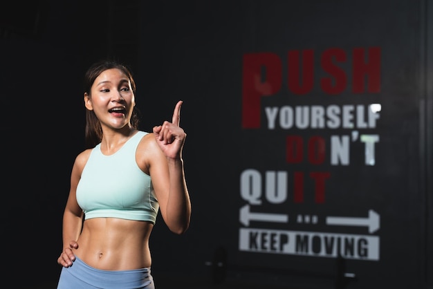 Lächelnde asiatische Sportlerin in sportlicher Kleidung, schlanker muskulöser Körper, der nach dem Training im Fitnessstudio posiert