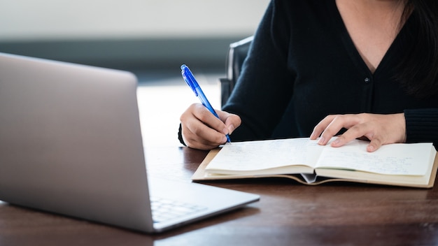 Lächelnde asiatische Studentin trägt drahtlose Kopfhörer, schreibt auf dem Notebook, um die Sprache online zu lernen, den Dozenten zu sehen und zu hören, Webinar per Videoanruf, E-Learning zu Hause, Fernunterricht