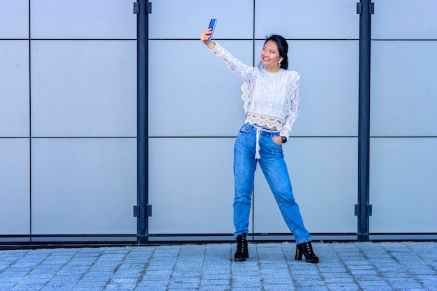 Lächelnde asiatische touristin mit drahtlosem headset und smartwatch macht ein selfie mit ihrem neuen telefon