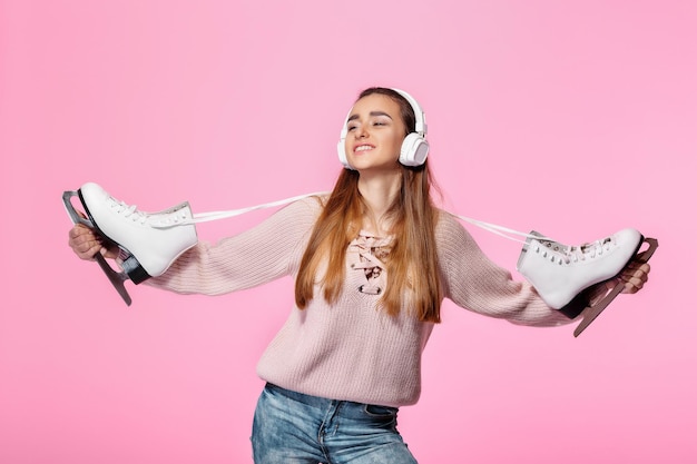 Lächelnde attraktive Frau, die Schlittschuhe hält und Musik über Kopfhörer hört