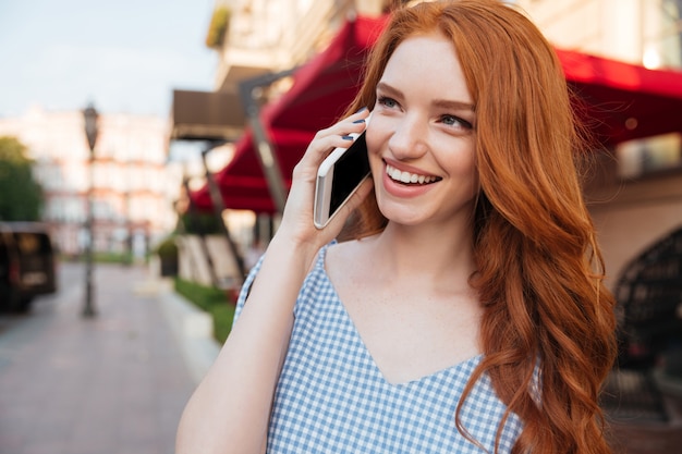 Lächelnde attraktive Frau mit langen Haaren, die auf Handy sprechen