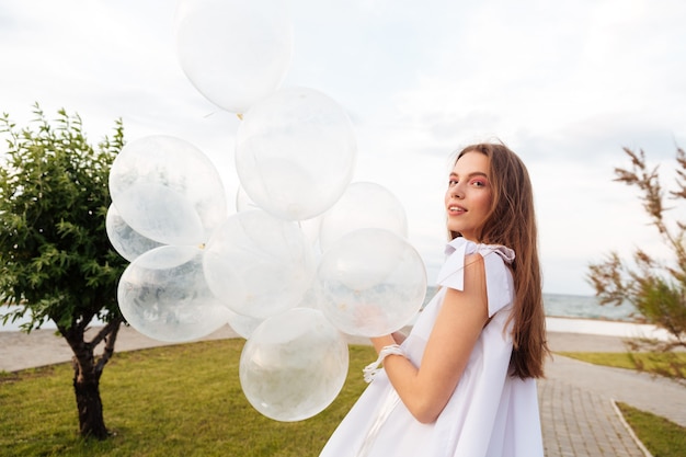 Lächelnde attraktive junge Frau mit Luftballons, die auf Promenade gehen