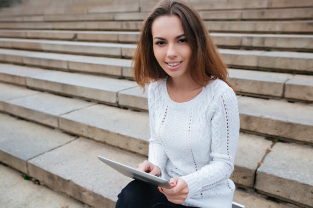 Lächelnde attraktive junge Frau mit Tablet auf Treppen im Freien