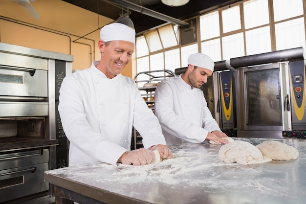 Lächelnde Bäcker, die Teig am Zähler kneten