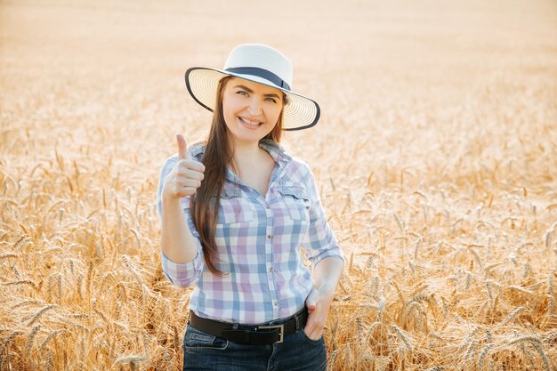 Lächelnde Bäuerin mit Hut, die Daumen nach oben zeigt und in die Kamera schaut, die Ackerland lächelnd...