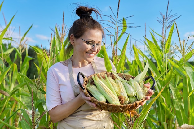 Lächelnde Bäuerin mit Korb mit frisch gepflücktem Mais