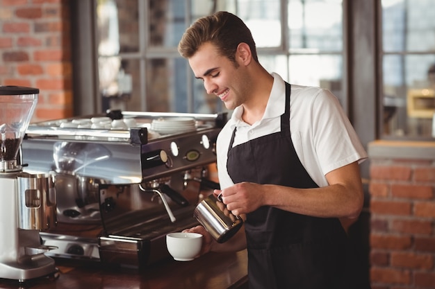 Lächelnde barista strömende Milch in Schale