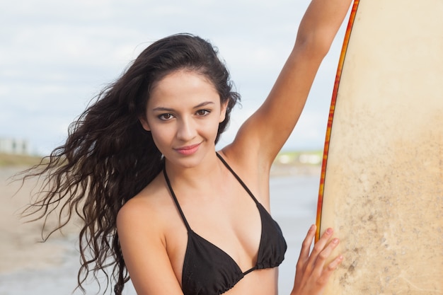Lächelnde Bikinifrau, die Surfbrett am Strand hält