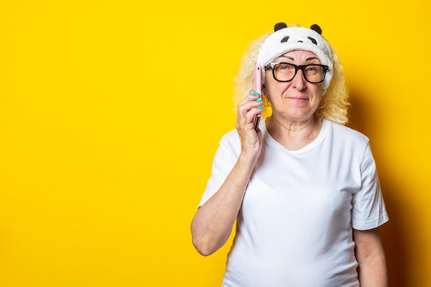 Lächelnde blonde alte Frau in der Schlafmaske, die Telefon hält