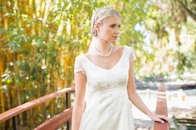Lächelnde blonde Braut in der Perlenhalskette, die auf einer Brücke steht