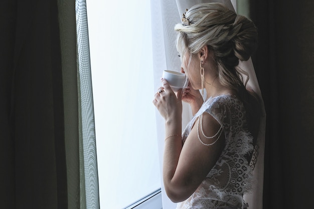 lächelnde blonde Braut in einem Hotelzimmer, das Kaffee trinkt