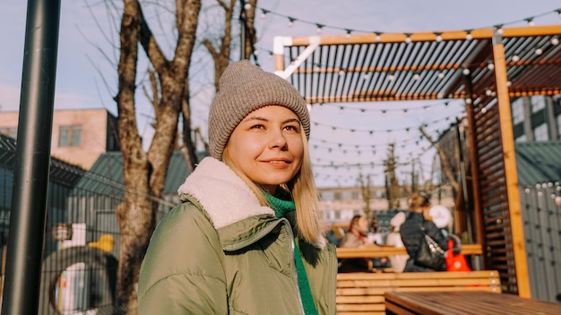 Lächelnde blonde Frau, die an einem Tisch in einem Straßencafé im städtischen Raum mit Street Food sitzt Warmer Wintertag, um Freunde zu treffen