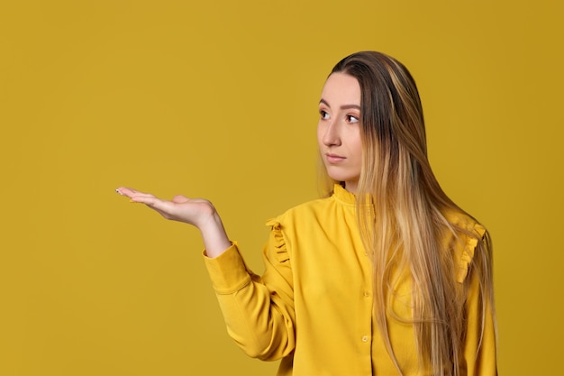 Lächelnde blonde Frau, die auf gelbem Hintergrund wegzeigt