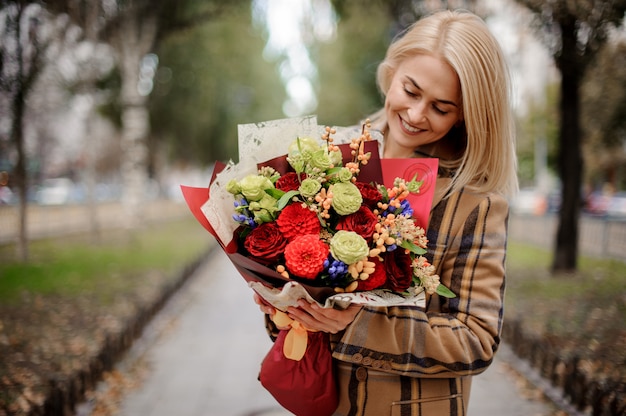 Lächelnde blonde Frau, die schönen Blumenstrauß im Herbstpark betrachtet