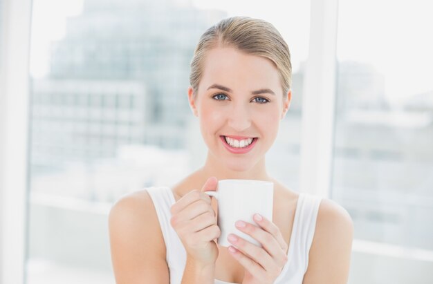 Lächelnde blonde Frau, die Tasse Kaffee hält