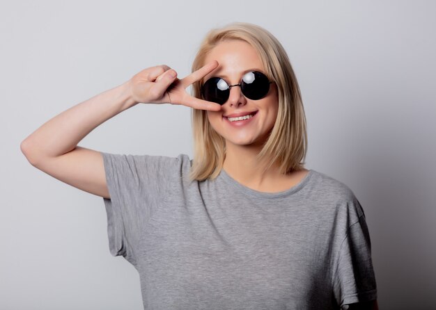 Lächelnde blonde Frau in der Sonnenbrille auf weißer Wand