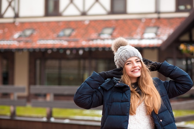 Lächelnde blonde Frau mit schwarzem Wintermantel und Strickmütze posiert auf der Straße in Kiew