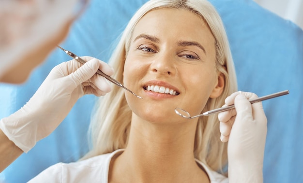 Lächelnde blonde Frau vom Zahnarzt in der Zahnklinik untersucht. Gesunde Zähne und Medizinkonzept.