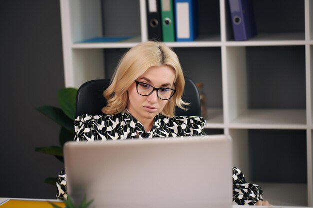 Foto lächelnde blonde geschäftsfrau mit brille und laptop im büro