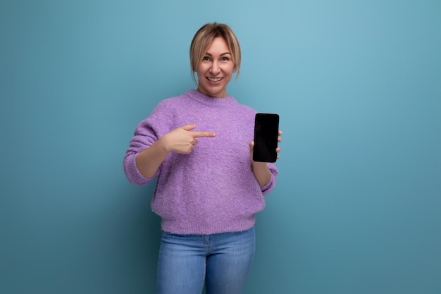 Lächelnde blonde junge Frau überraschte das Halten des Smartphonemodells auf hellem buntem Hintergrund