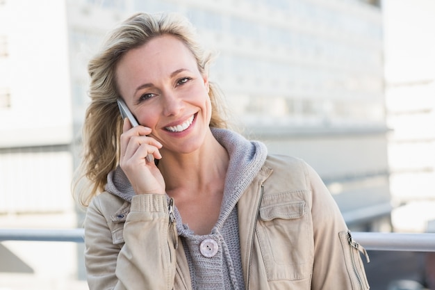 Lächelnde blonde Stellung am Telefon