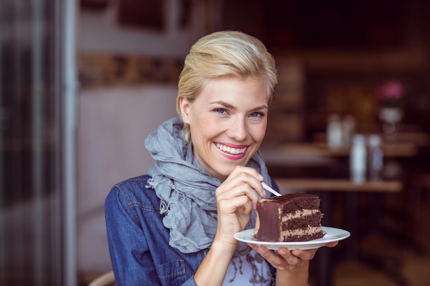 Lächelnde Blondine, die ein Stück Schokoladenkuchen nimmt