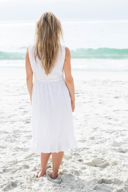 Lächelnde Blondine im weißen Kleid, welches das Meer bereitsteht