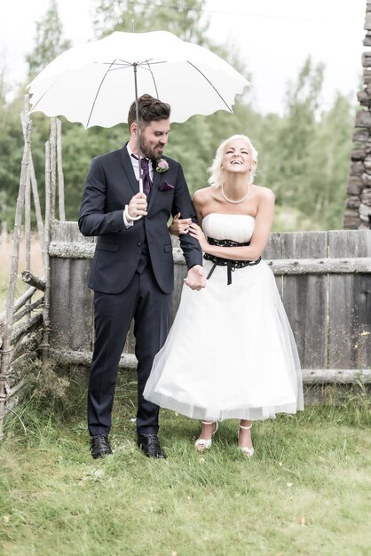 Foto lächelnde braut und bräutigam stehen mit einem regenschirm auf dem hof