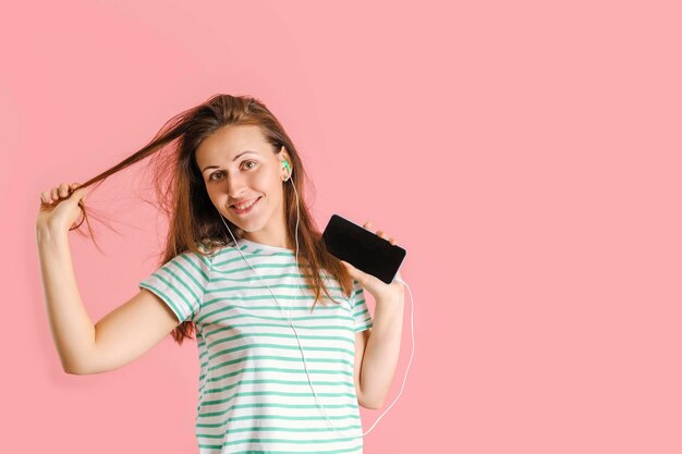Lächelnde Brünette tanzt Musik hören mit Kopfhörern auf rosa Hintergrund. Exemplar