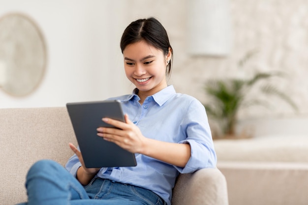 Lächelnde Dame, die mit einem digitalen Tablet auf dem Sofa sitzt