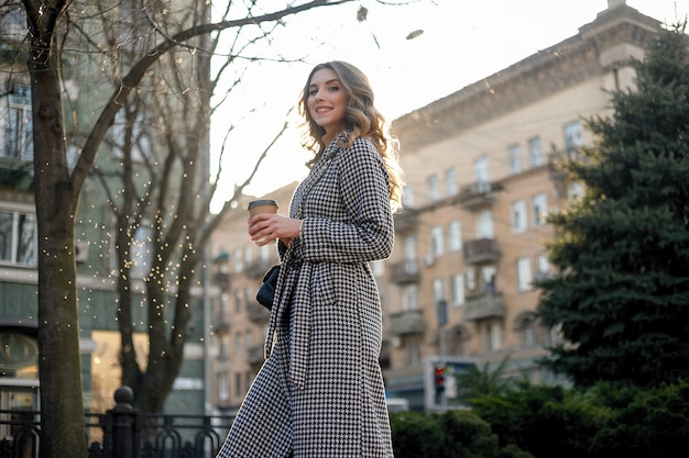 Lächelnde elegante Frau im Trenchcoat, die das Handy hält