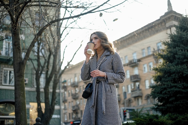 Lächelnde elegante Frau im Trenchcoat, die Kaffeetasse hält holding