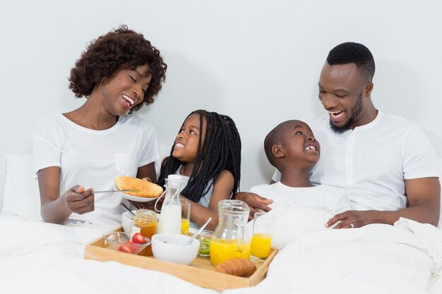 Lächelnde Eltern und Kinder frühstücken im Schlafzimmer