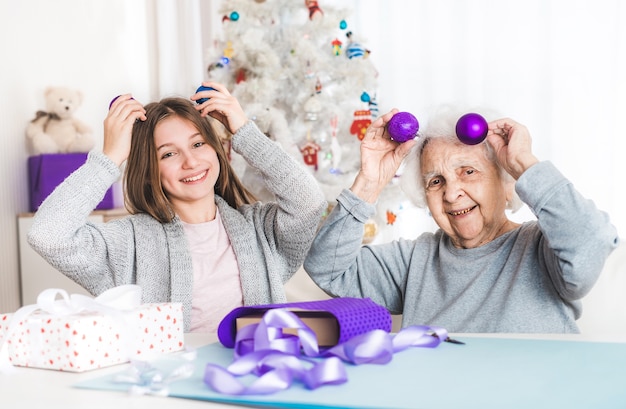 Lächelnde Enkelin ang Oma spielt mit dekorativen Bällen zu Weihnachten
