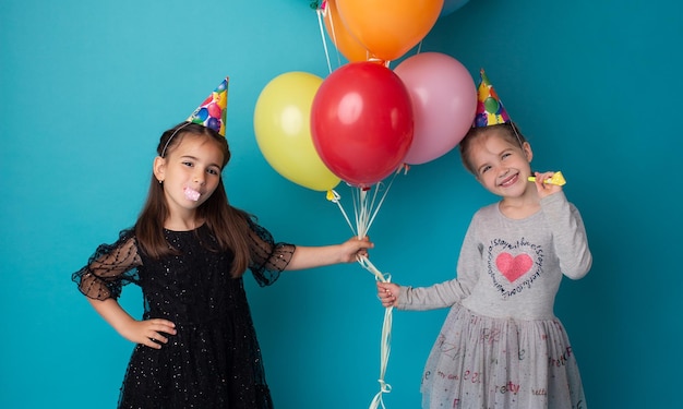 Lächelnde entzückende kleine Kindermädchen, die mit farbigen Luftballons auf blauem Hintergrund posieren