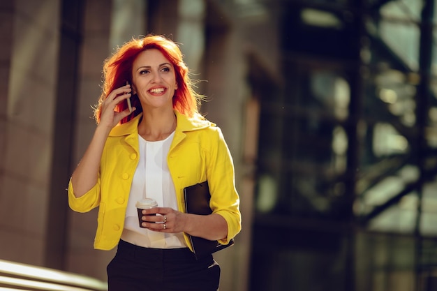 Lächelnde erfolgreiche Geschäftsfrau mit Smartphone in einer Kaffeepause im Büroviertel. Wegschauen.