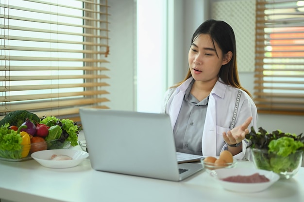 Lächelnde Ernährungswissenschaftlerin ruft Patienten an und gibt Online-Konsultationen über Laptop Gesundheitsversorgungskonzept