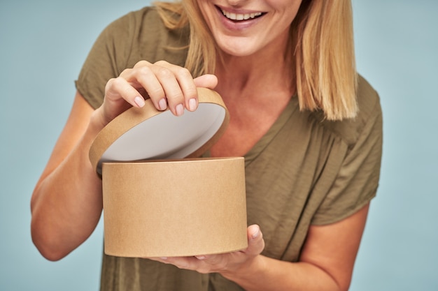 Lächelnde erwachsene Frau, die in die Geschenkbox schaut und sich wundert