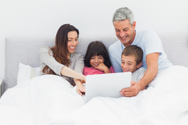 Lächelnde Familie, die im Bett unter Verwendung ihres Laptops liegt