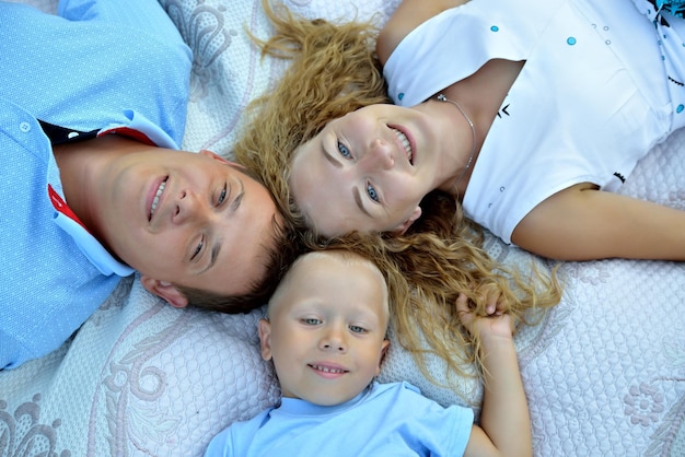 Foto lächelnde familie mama papa baby liegt auf einer decke und schaut in die kamera sonniger sommertag