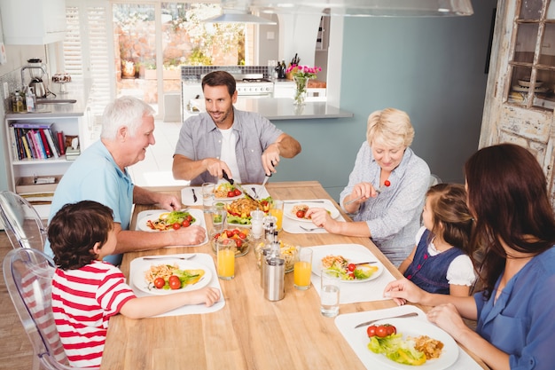 Lächelnde Familie mit den Großeltern, die am Speisetische sich besprechen